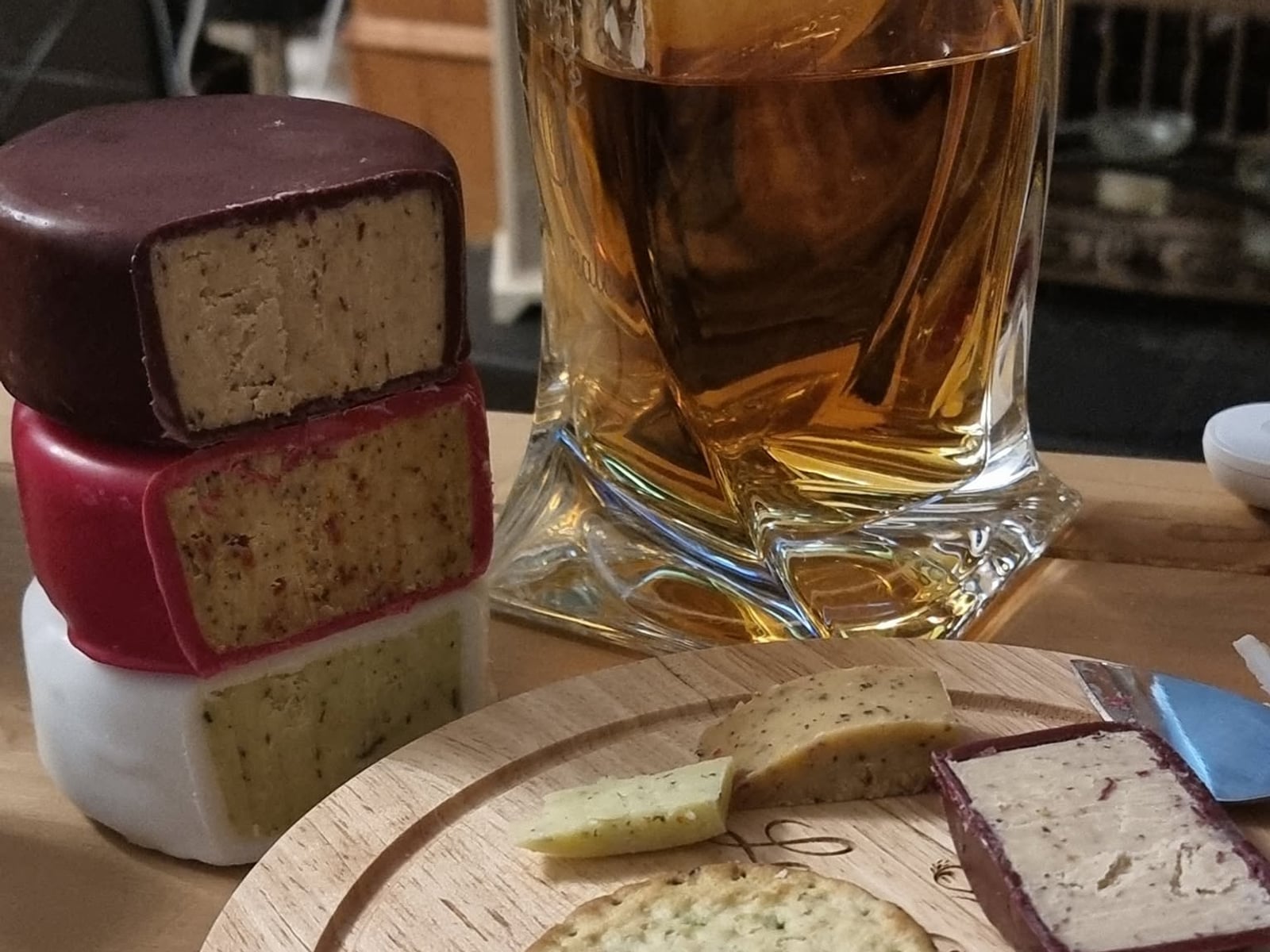 Three waxed cheddar truckles stacked and cut open, beside a glass and a wooden board with crackers